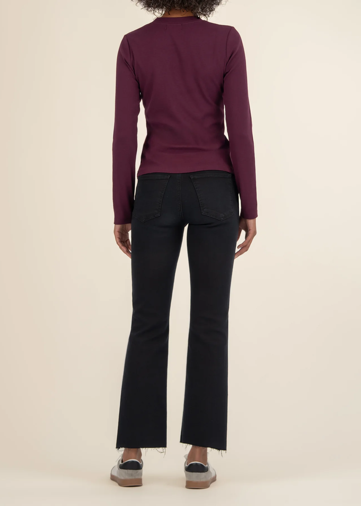 Woman turned around wearing a maroon long sleeve tee with black jeans and white sneakers in front of a white background