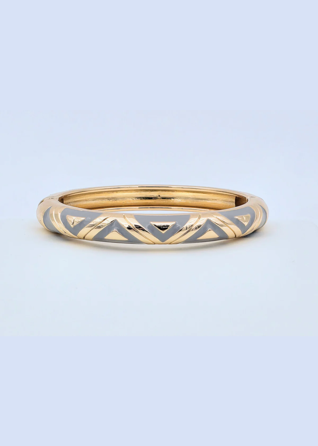 Gold and grey geometric pattern bangle bracelet on a blue background