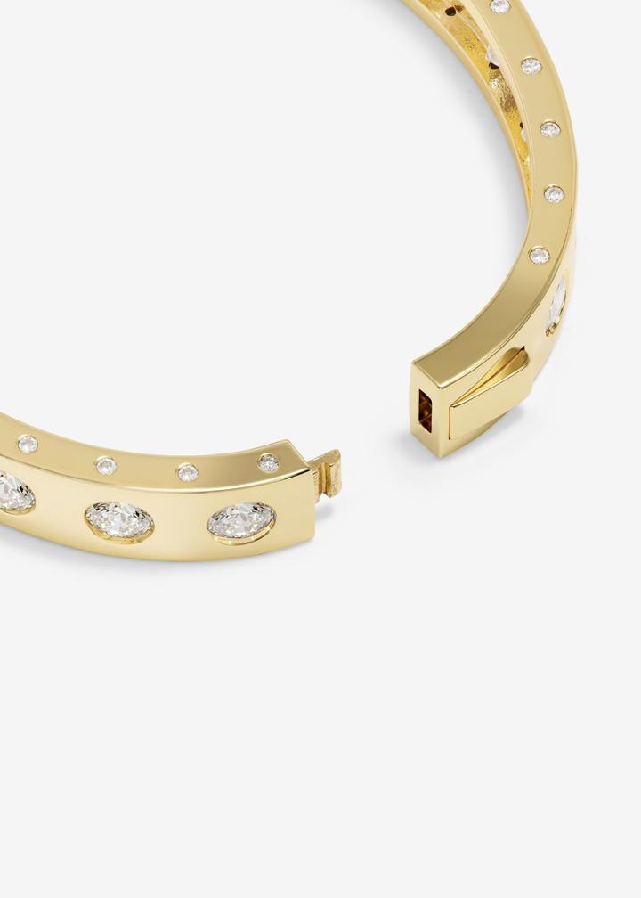 Close up of a gold cuff bracelet with CZ studding on a white background