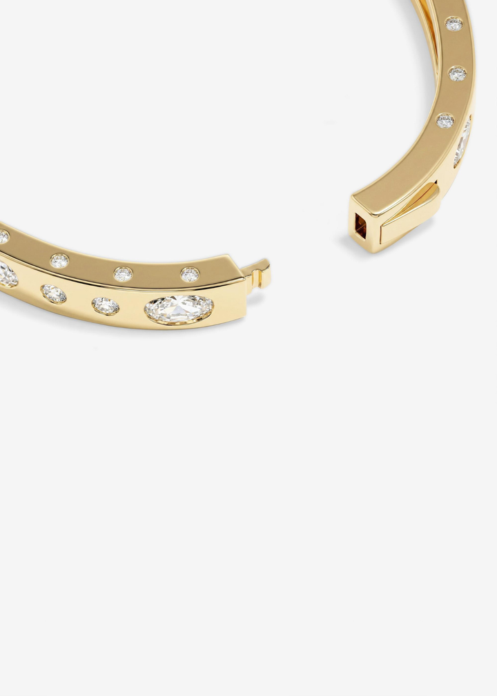 Close up of a gold cuff bracelet with CZ studding on a white background