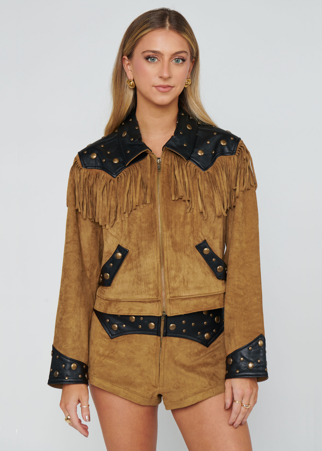 Woman wearing a brown suede jacket with black leather accents and fringe on a white background