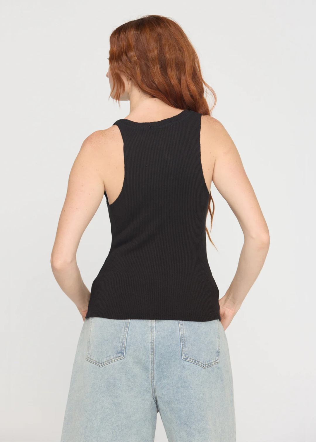Woman turned around wearing a notch neck black tank top with denim shorts and a belt