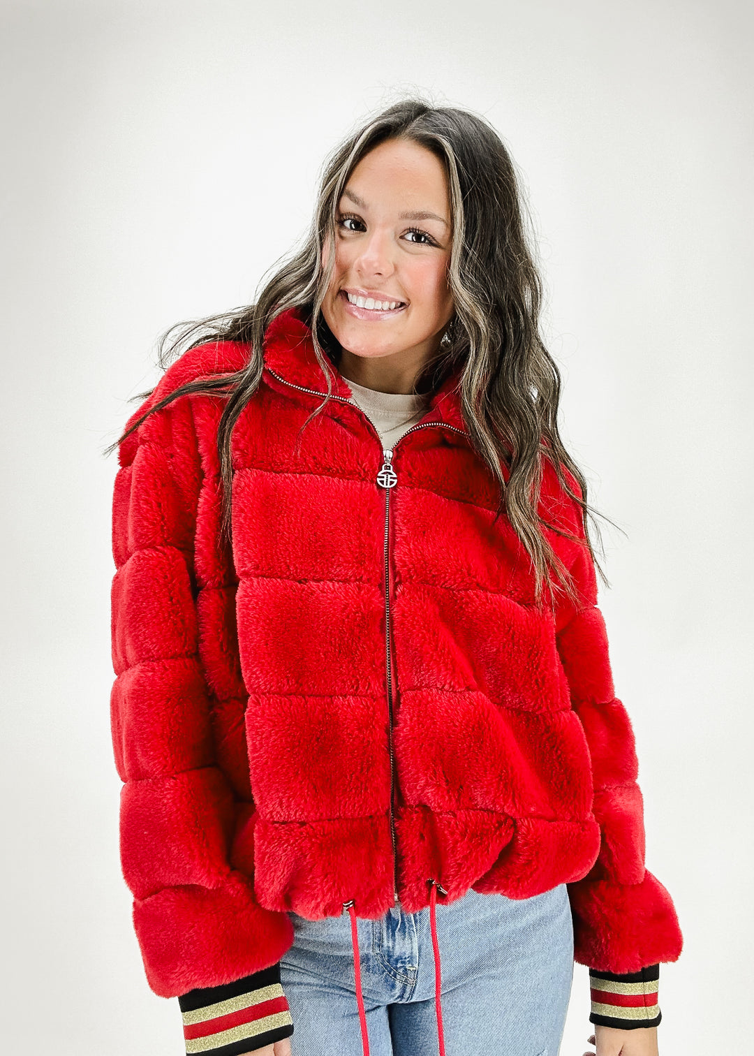 A woman wearing a red faux fur jacket with zipper closure and a drawstring hem, styled with light-wash jeans for a cozy and bold winter look.