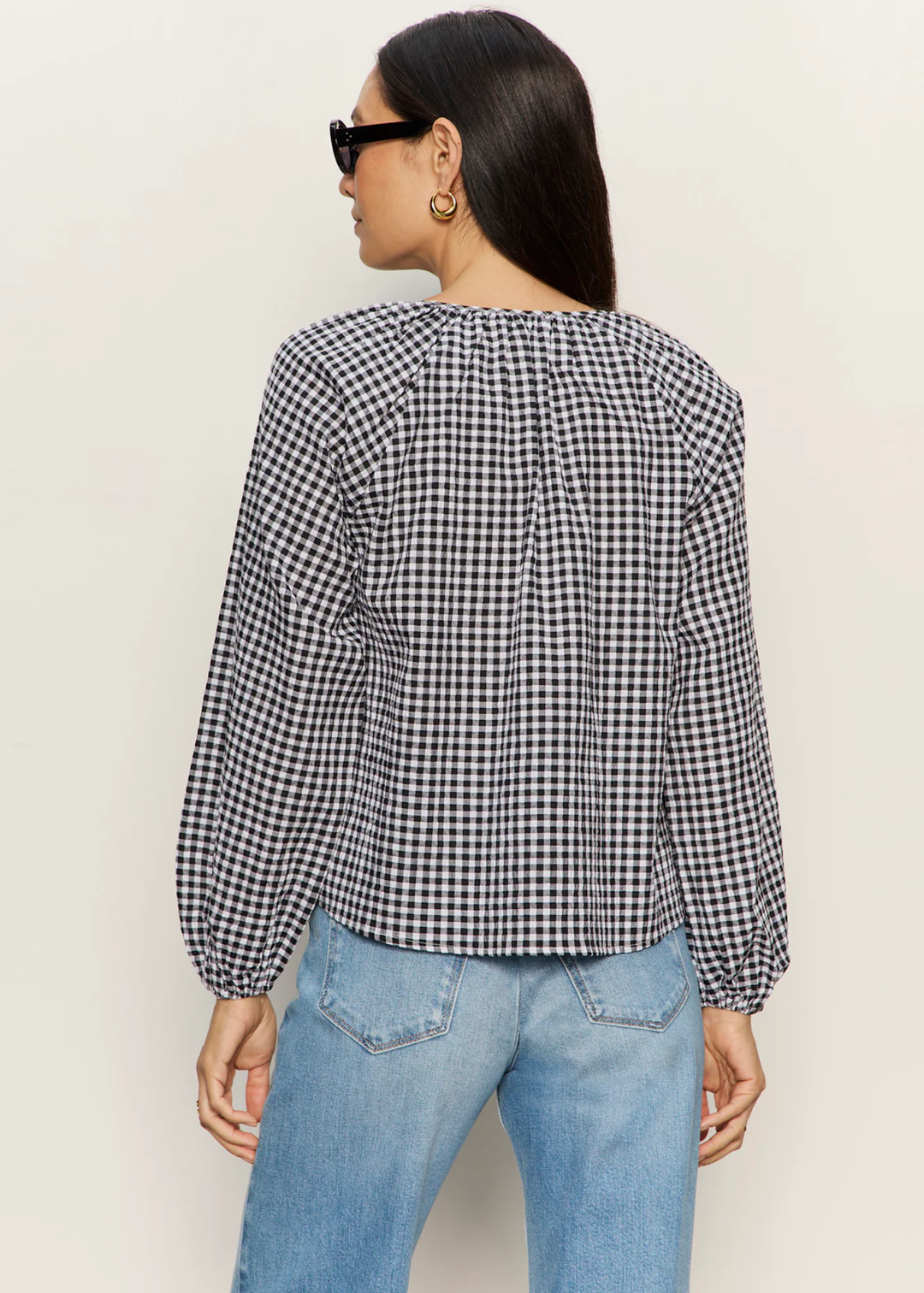 Woman turned around wearing a black and white gingham top with jeans