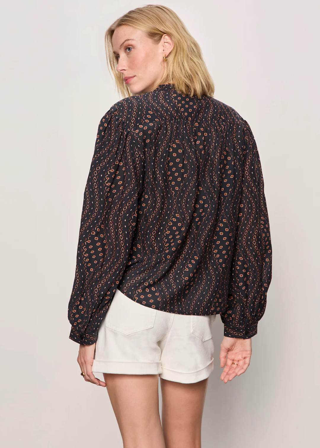 Woman turned around wearing a black and brown patterned blouse with white shorts