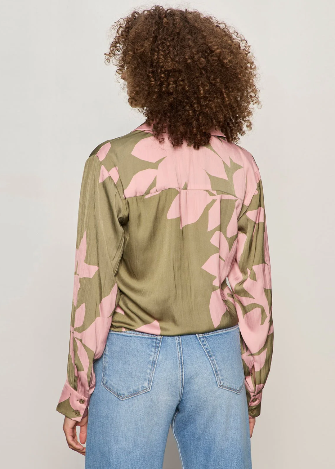 Woman turned around wearing a green and pink floral button down tie front shirt with jeans