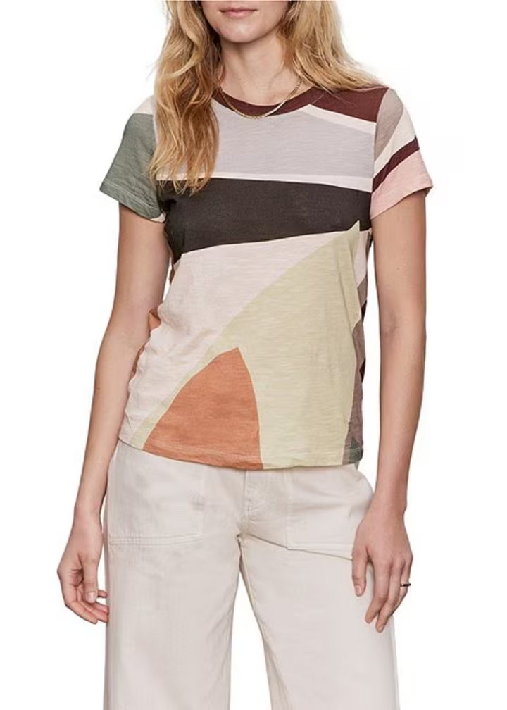 Woman wearing a multi color t-shirt and white pants in front of a white background