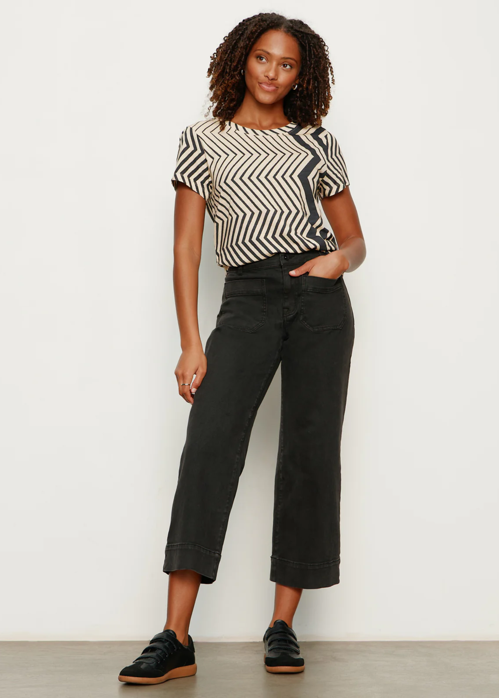 Woman with hand in pocket wearing a t-shirt with white and black zig zag stripes with black jeans