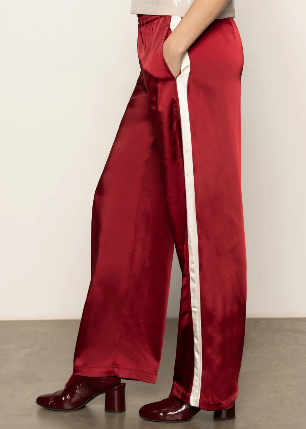 Woman turned to the side wearing red satin pants with a white side stripe and black boots