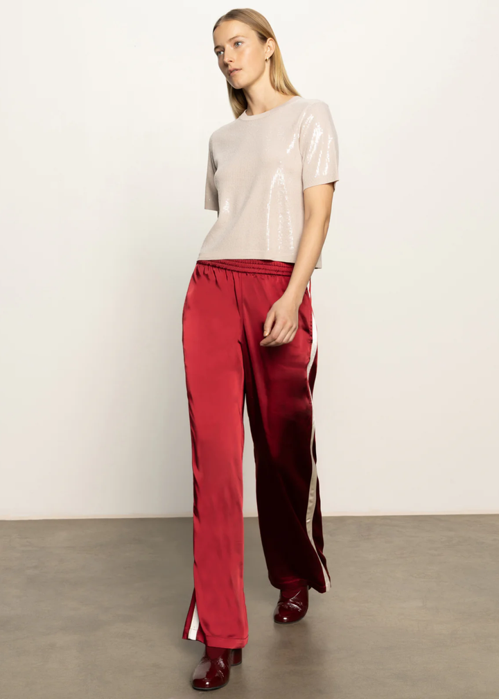 Woman wearing red satin pants with a white side stripe and a tan sequined top and black boots