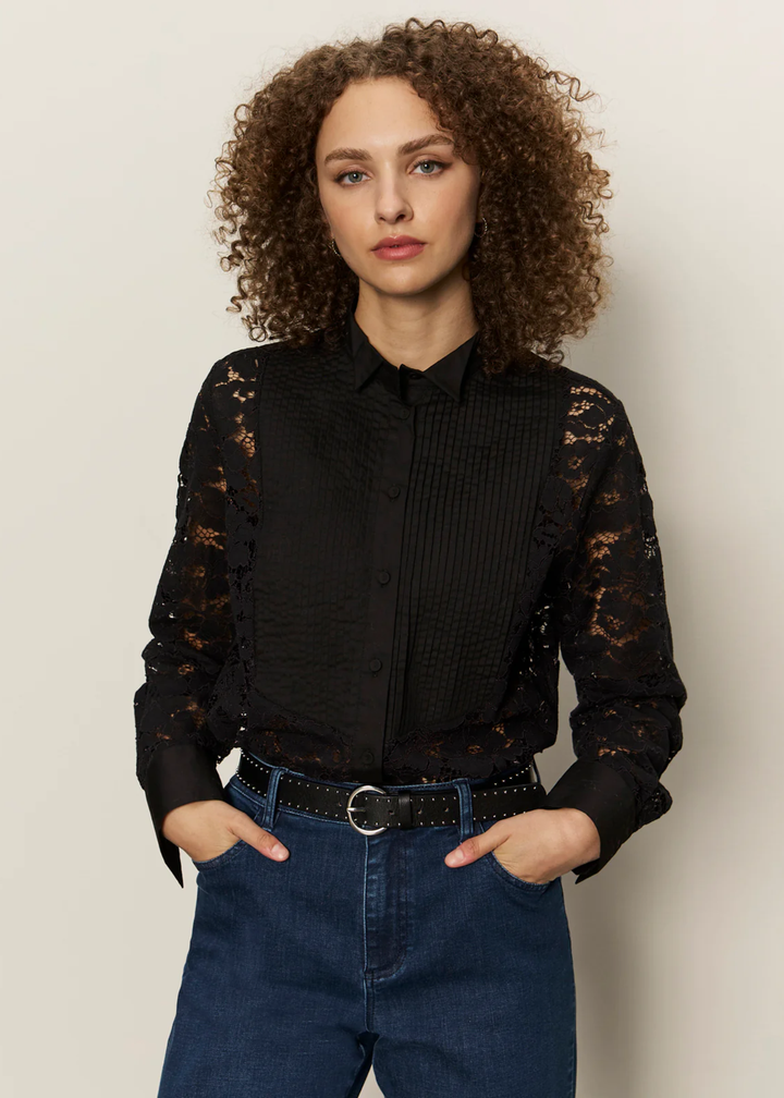 Woman wearing a black button down shirt with lace sleeves and back with jeans against a white background