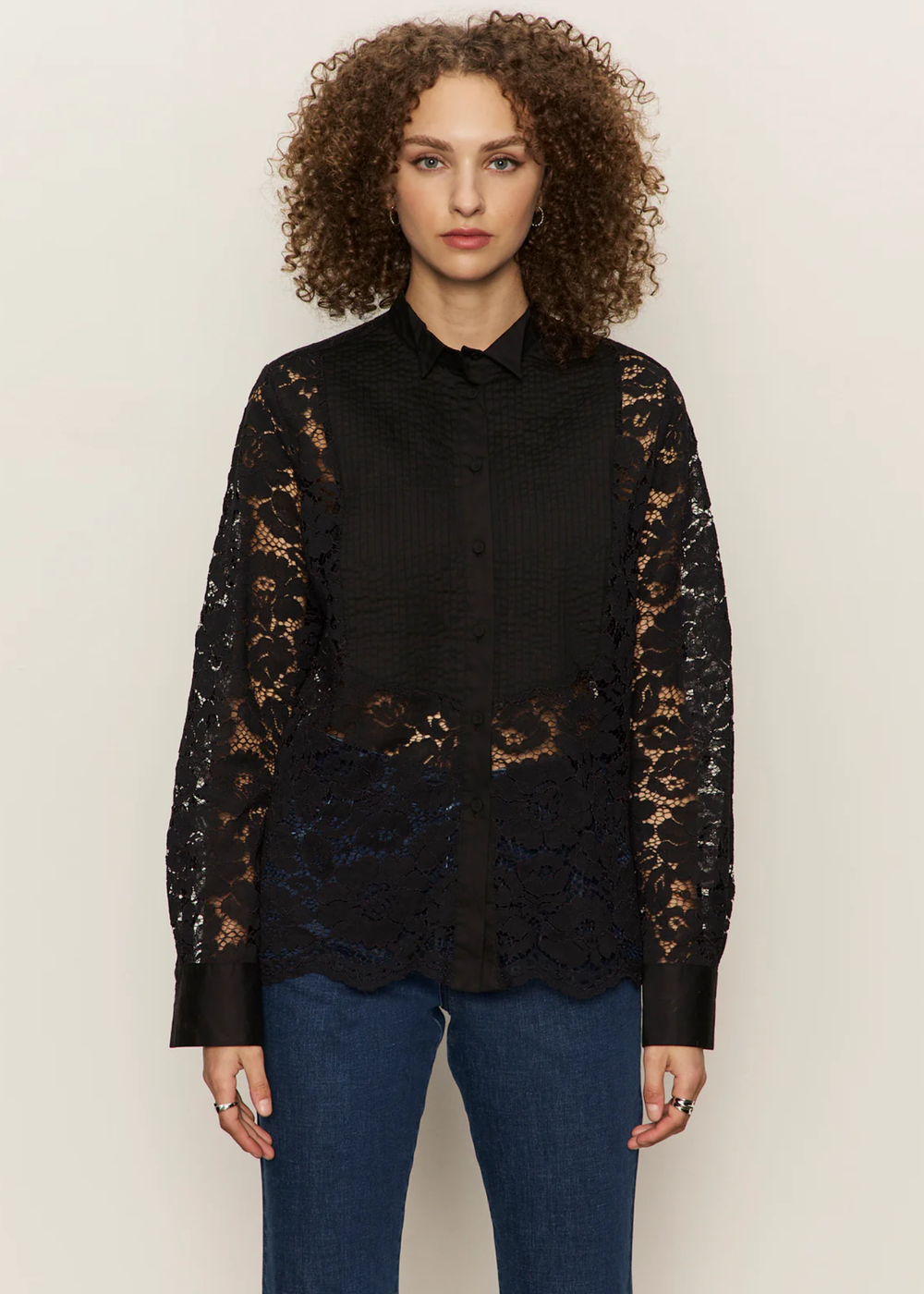 Woman wearing a black button down shirt with lace sleeves and back with jeans against a white background
