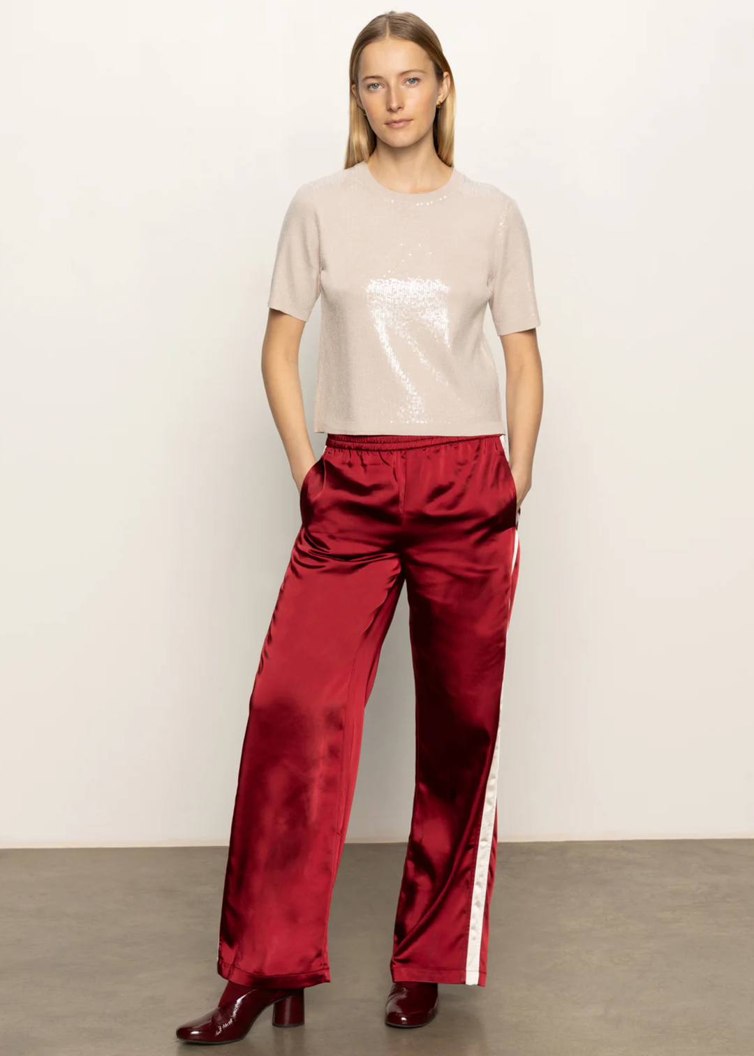 Woman wearing a cream sequined short sleeve top with red satin pants standing in front of a white background
