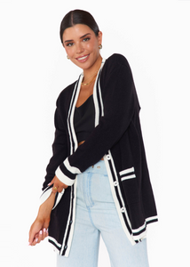 black mid thigh length cardigan with white varsity stripe trim, pockets, and cuffs with white buttons up front