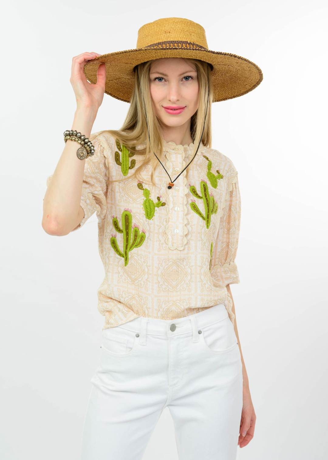 Woman wearing a tan top with cactus embroidery and white jeans