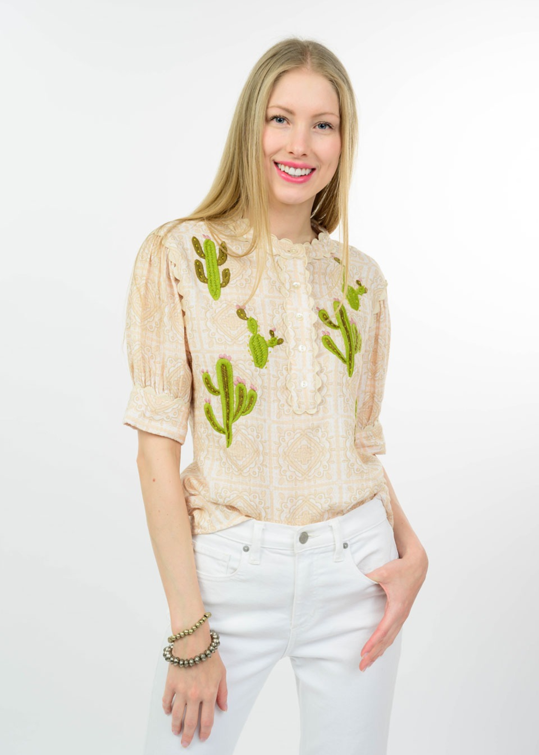 Woman wearing a tan top with cactus embroidery and white jeans