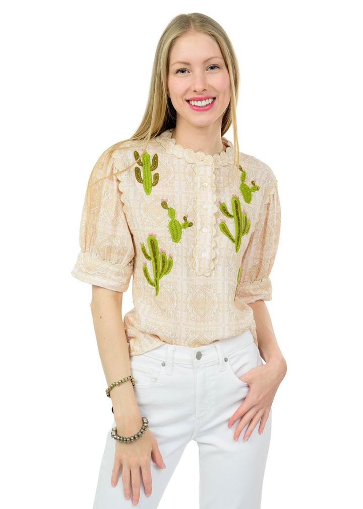 Woman wearing a tan top with cactus embroidery and white jeans