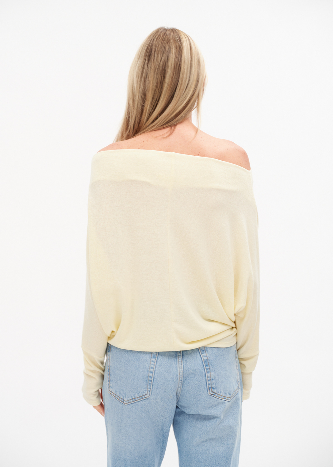 Woman turned around wearing an off the shoulder yellow top with jeans