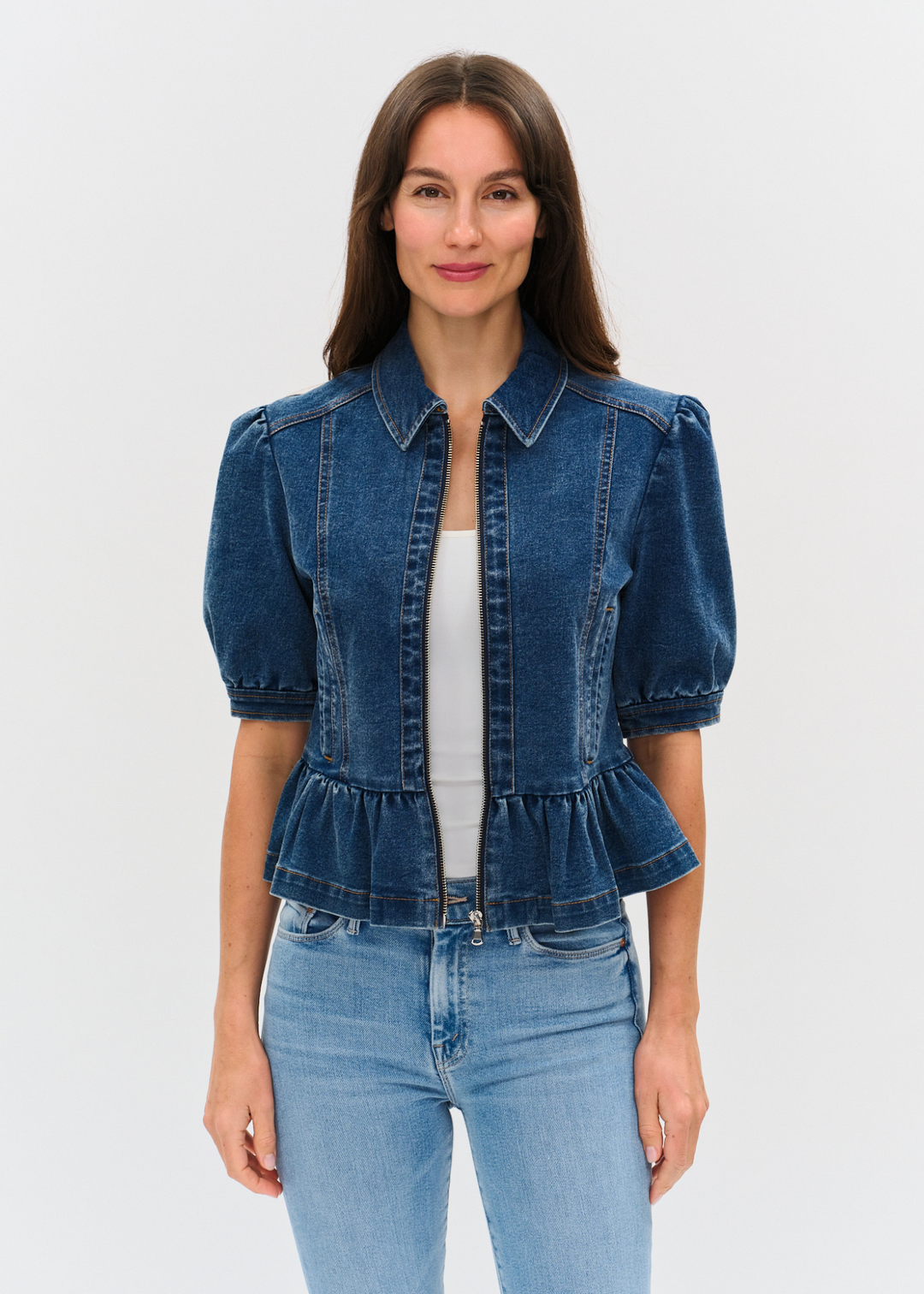 Woman wearing a dark denim jacket with puff sleeves and a peplum design over a white shirt and light wash jeans