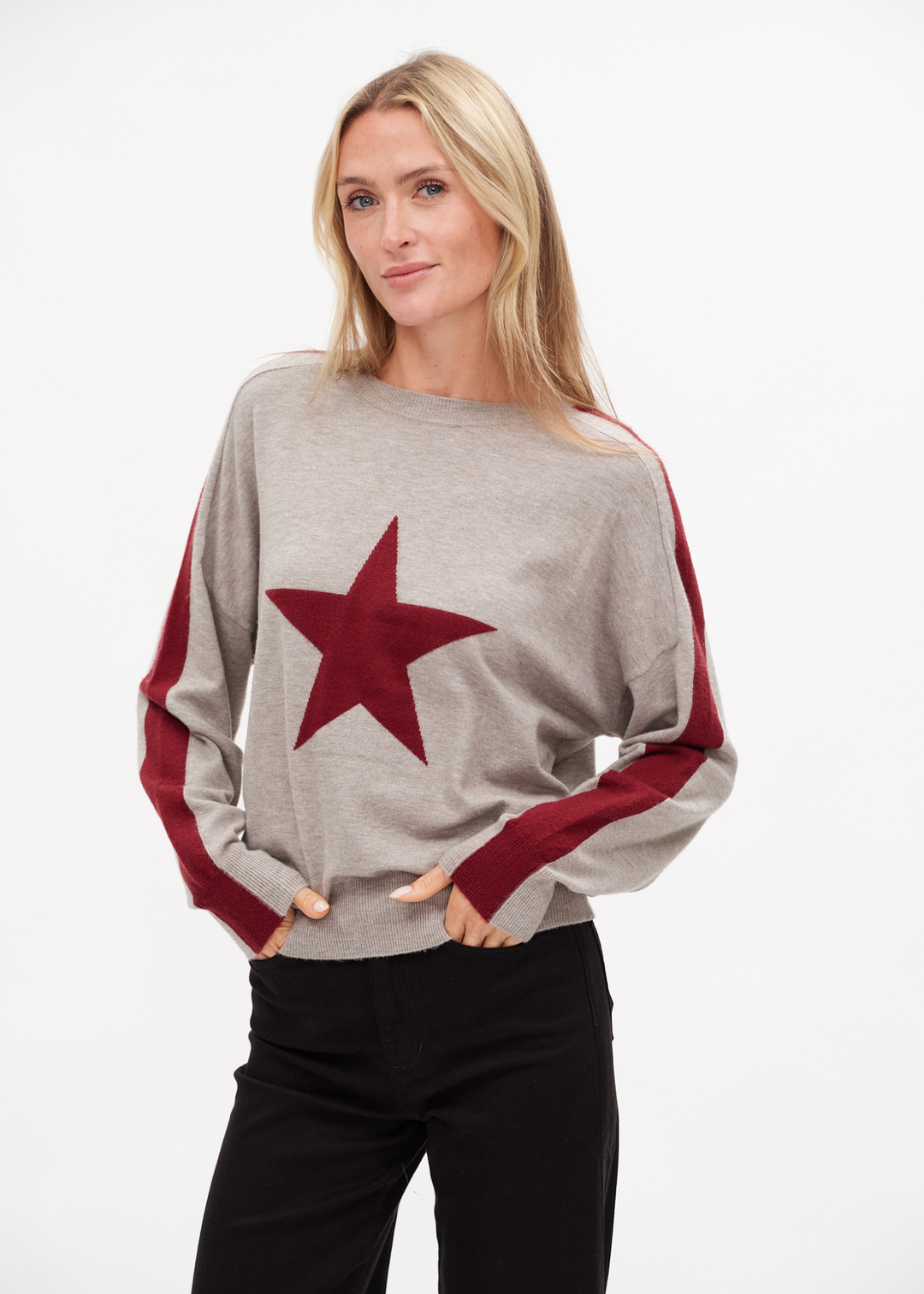 Woman wearing a grey sweater with a red star and sleeve stripes against a white background