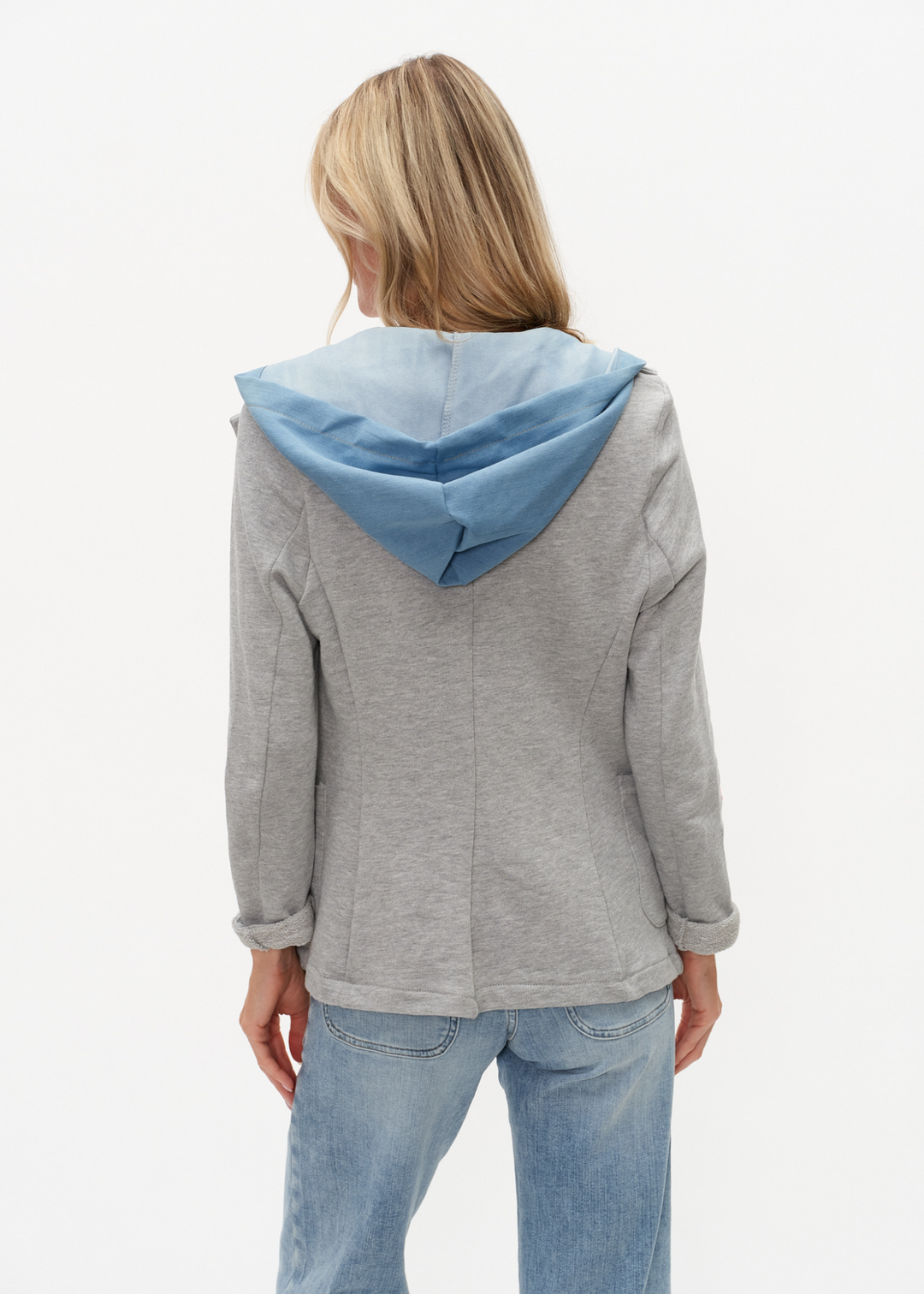Woman turned around wearing a denim and grey knit hooded blazer with jeans