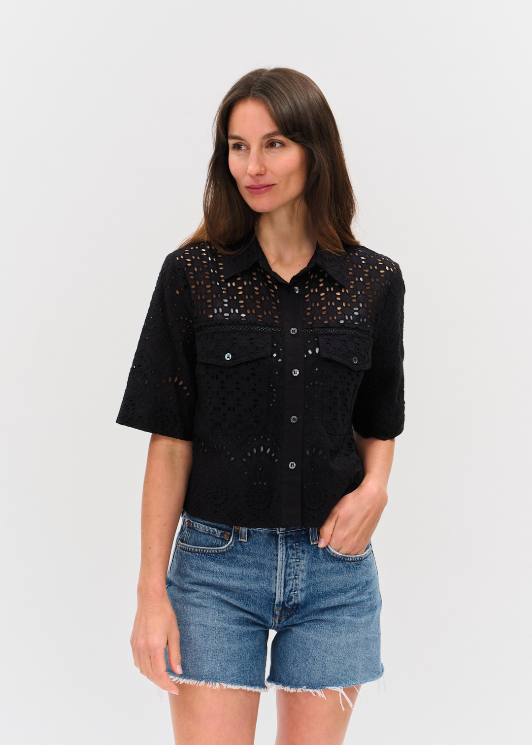 Woman wearing a black eyelet button down top with denim shorts