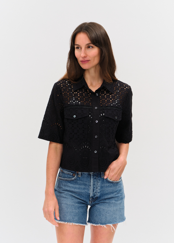 Woman wearing a black eyelet button down top with denim shorts
