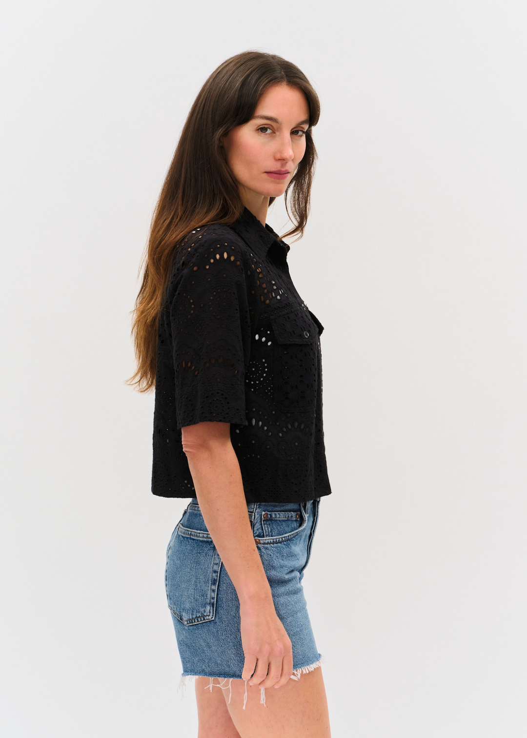 Woman turned to the side wearing a black eyelet button down top with denim shorts