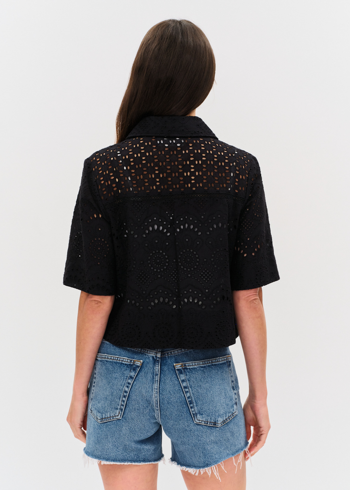 Woman turned around wearing a black eyelet button down top with denim shorts