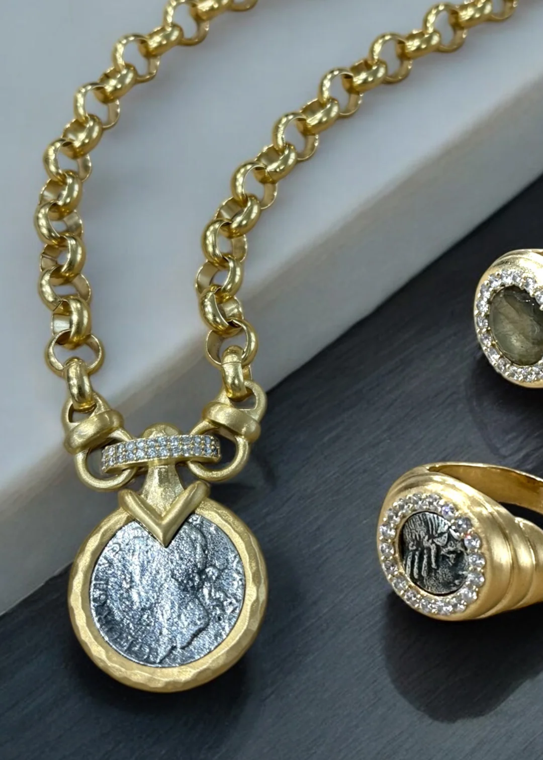 Gold chain necklace with a silver coin pendant on a grey background