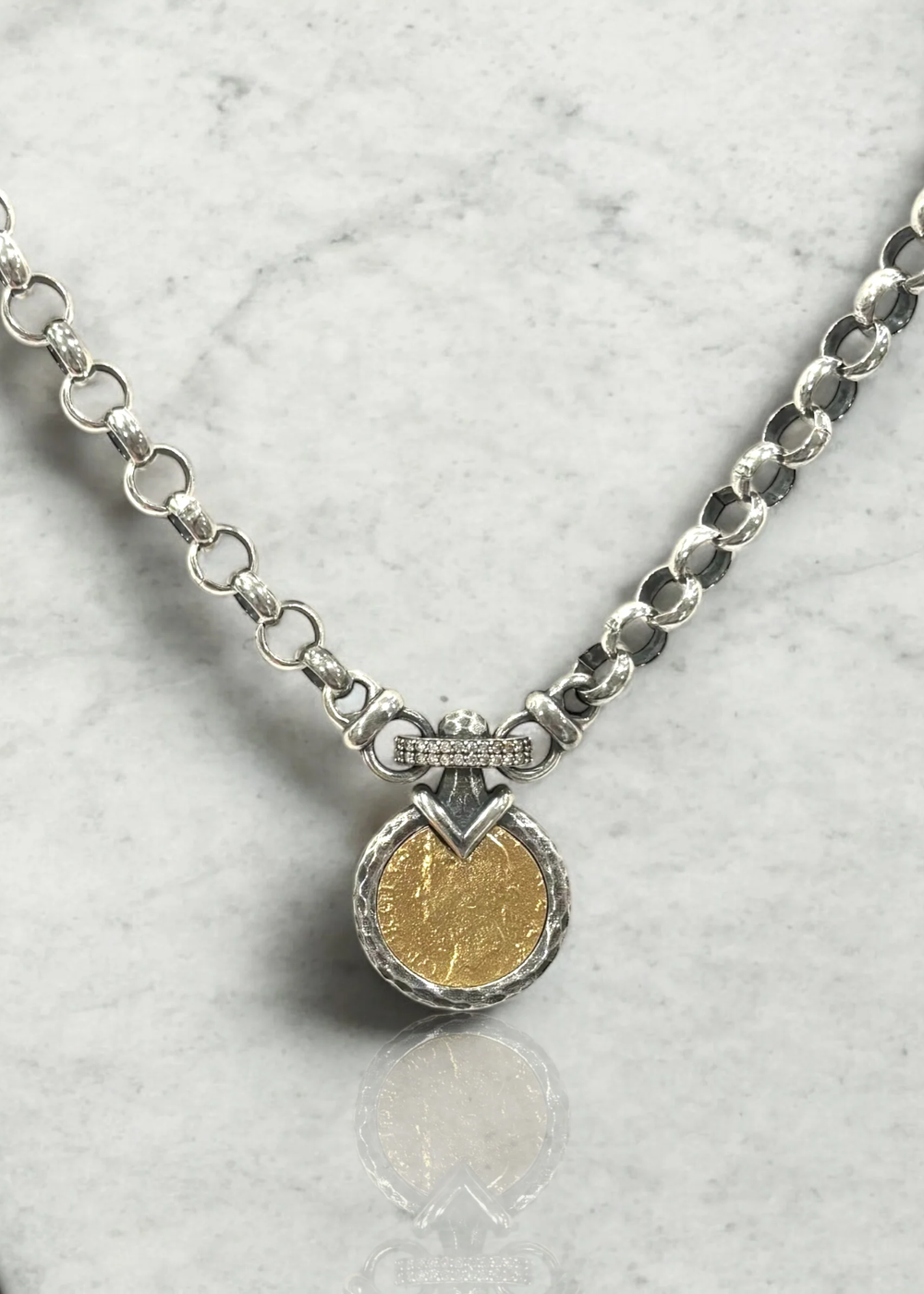 A vintage silver chain necklace with a gold coin pendant on a white background