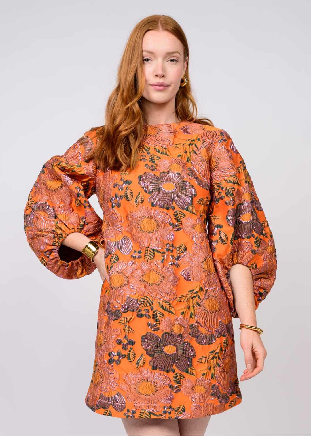 Woman wearing an orange mini dress with a floral pattern against a white background