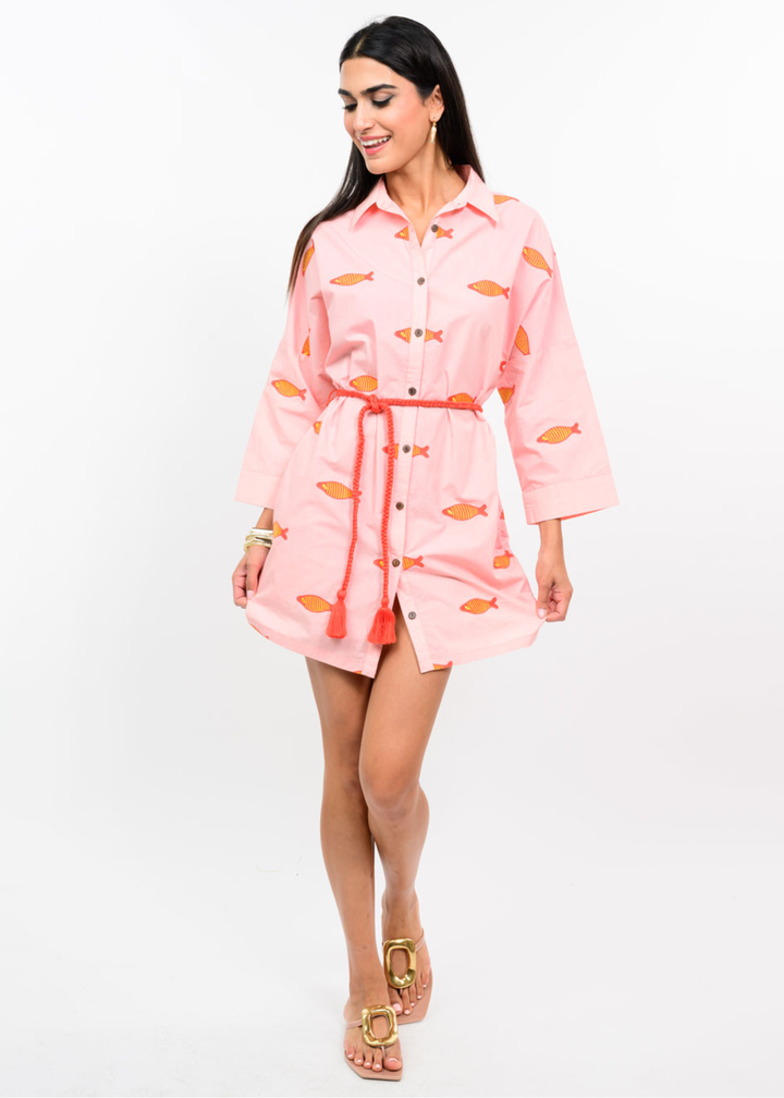 Woman wearing a blush colored dress with a fish pattern and a pink belt