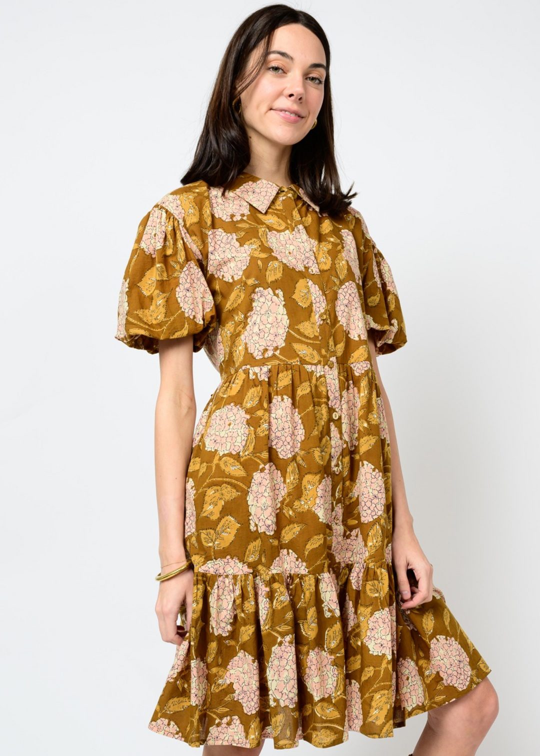 Woman wearing a brown dress with a floral pattern, puff sleeves, and a collared neckline