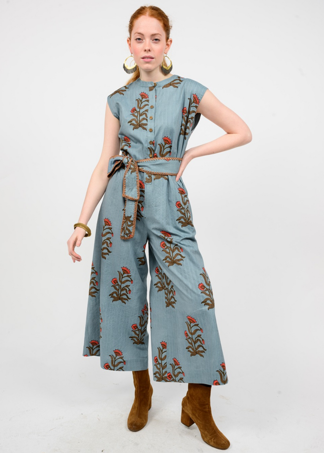 Woman wearing a blue jumpsuit with a green and red floral print and belt