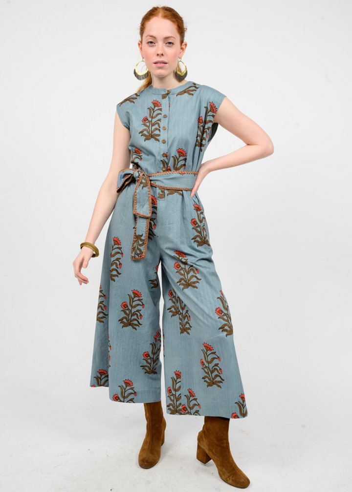 Woman wearing a blue jumpsuit with a green and red floral print and belt