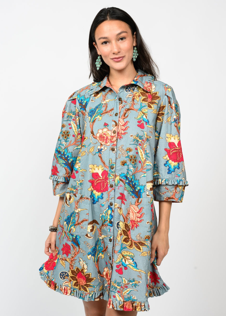 Woman wearing a medium blue dress with a multicolor floral pattern in front of a white background