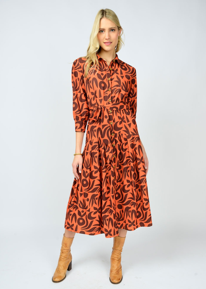 Woman wearing an orange and brown patterned midi dress with light brown boots in front of a white background