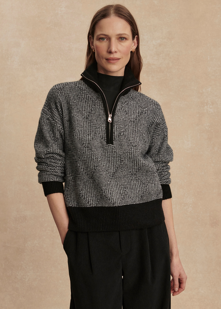 Woman wearing a black knit top with black pants against a tan background