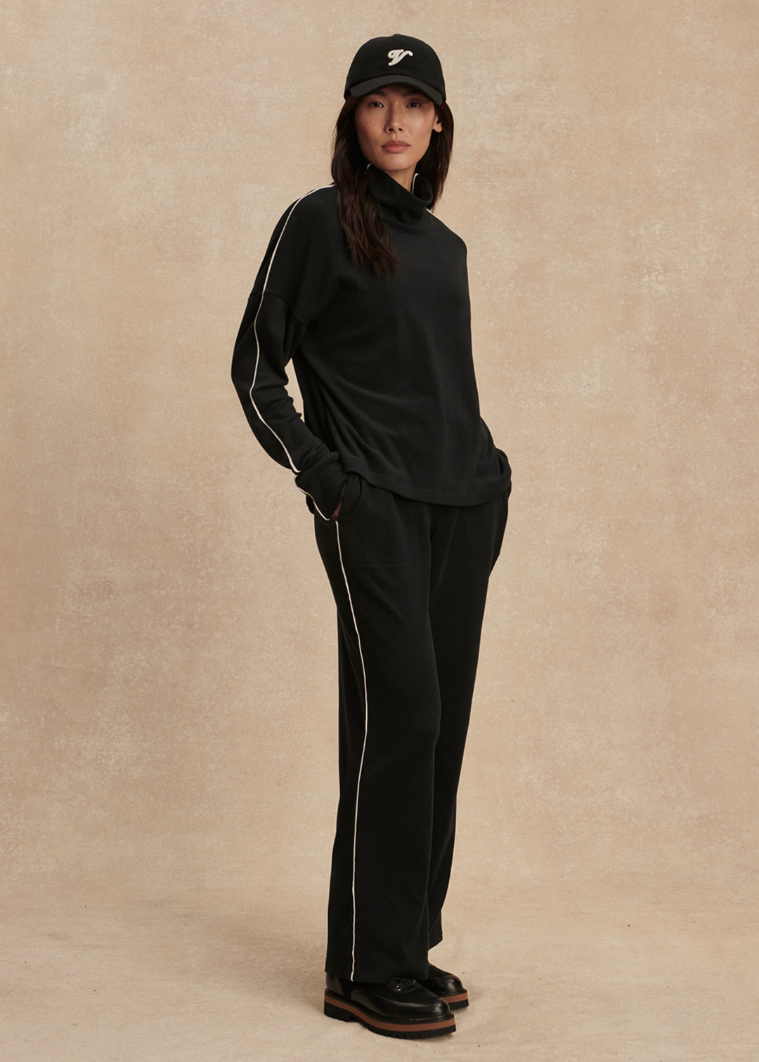 Woman turned to the side wearing a black top and black pants against a tan background