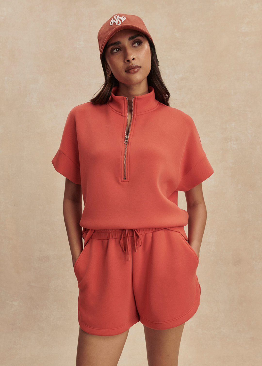 Woman wearing orange shorts with a half zip top