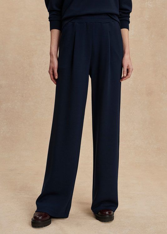 Woman wearing wide leg navy sweatpants with a matching top in front of a tan background