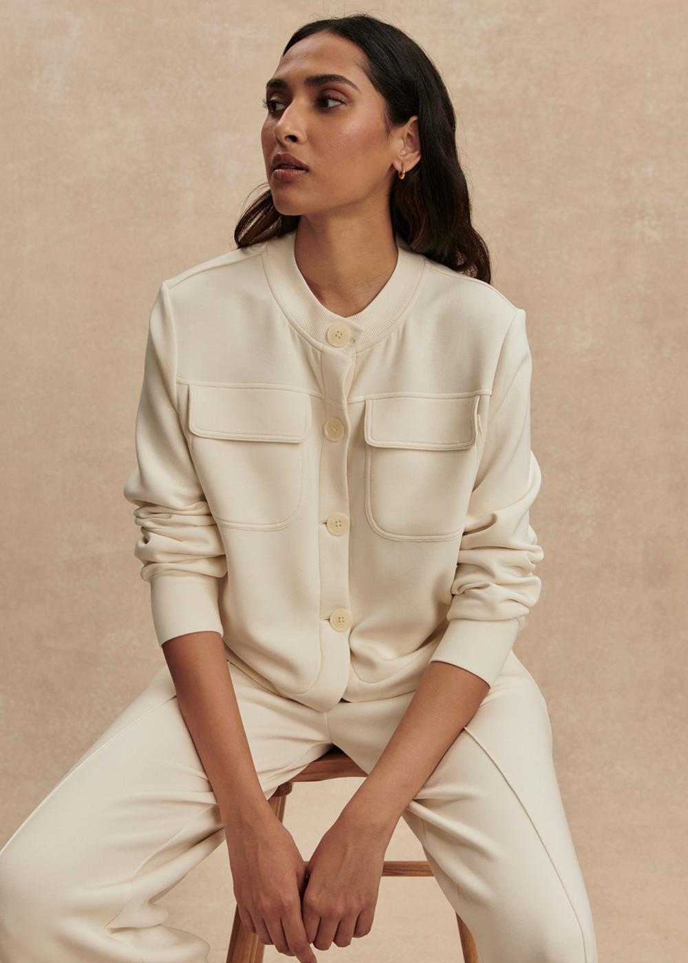 Woman wearing a cream button down sweater with matching pants against a tan background
