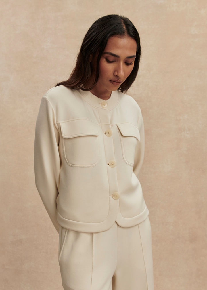 Woman wearing a cream button down sweater with matching pants against a tan background