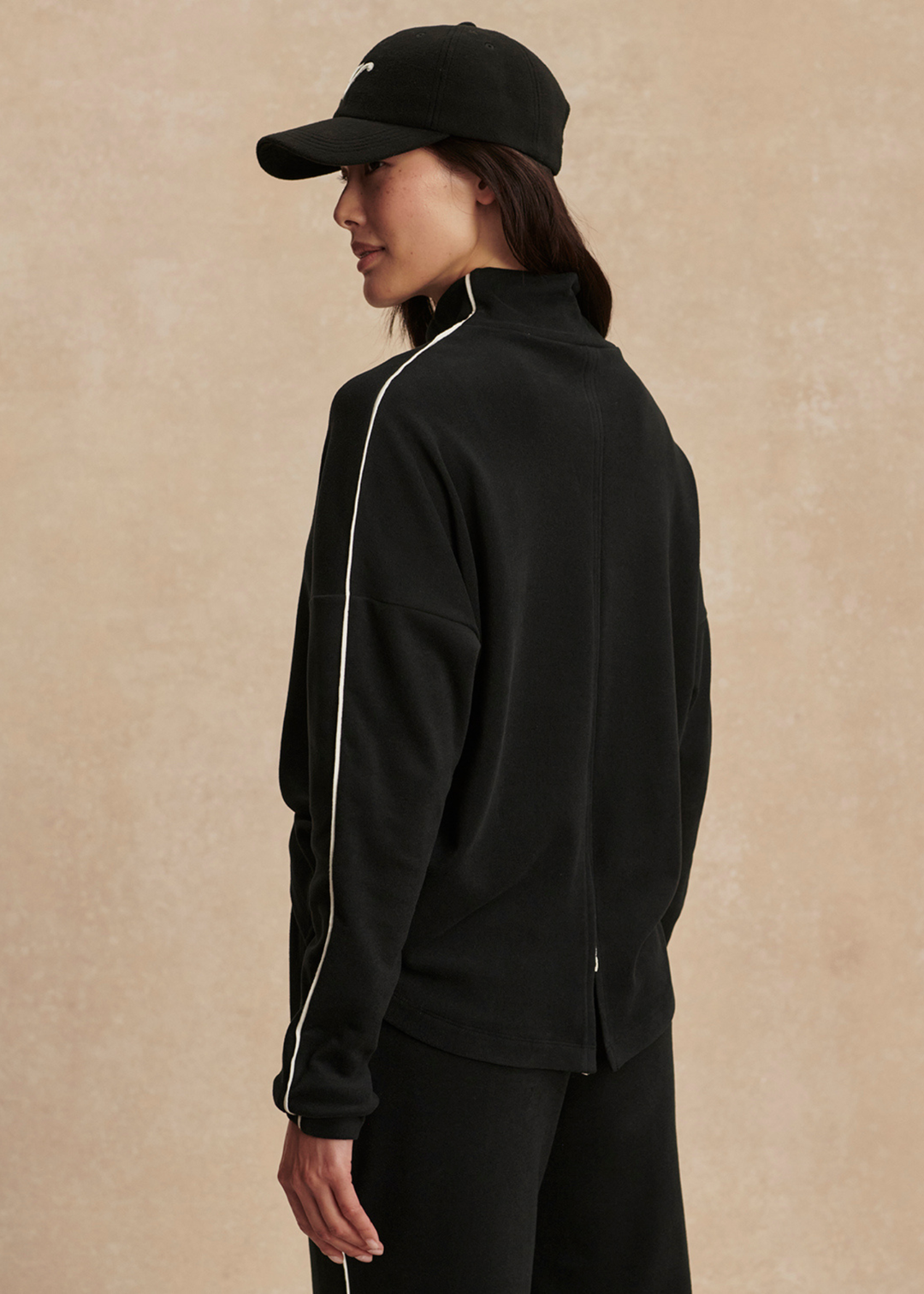 Woman turned to the side wearing a black set with white trim against a tan background