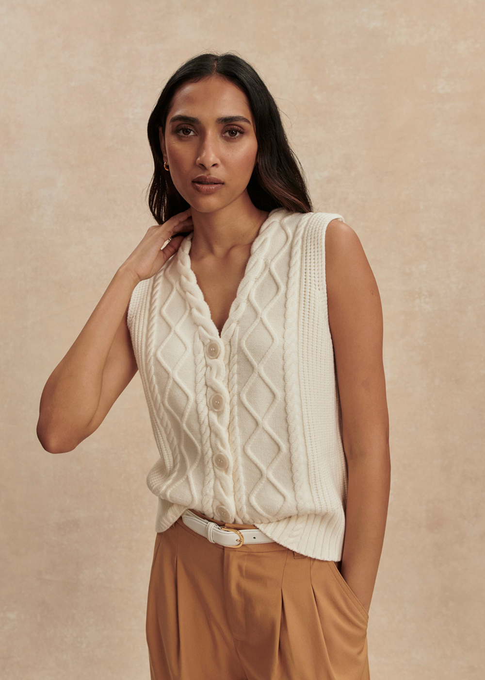 Woman wearing a cream cable knit sweater vest with brown pants