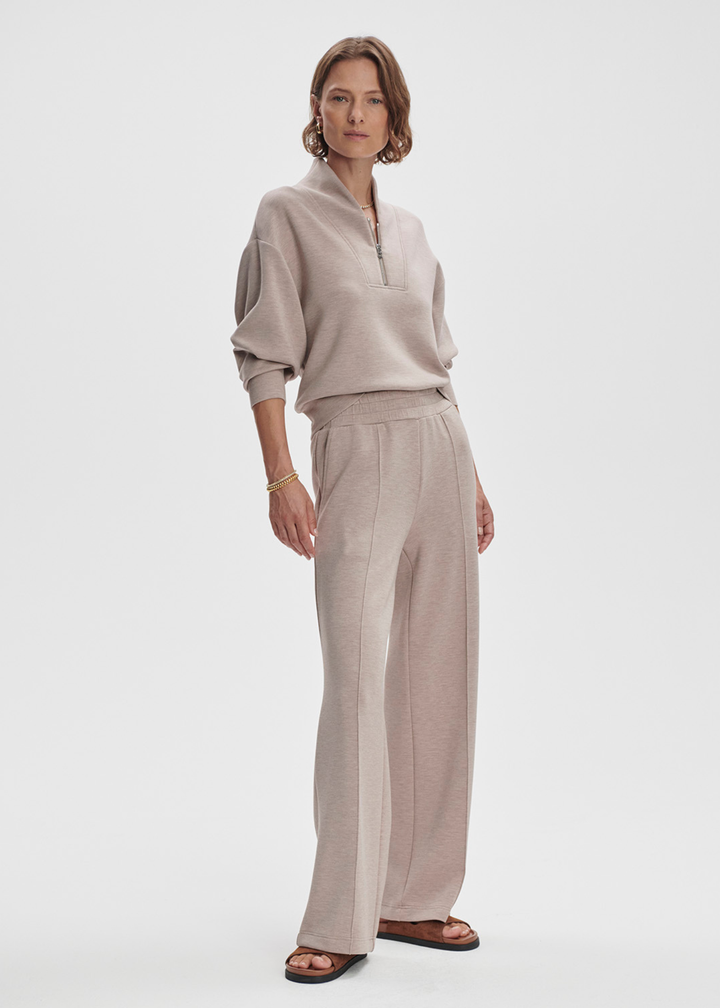 Woman wearing taupe wide leg pants with a taupe half zip top against a white background