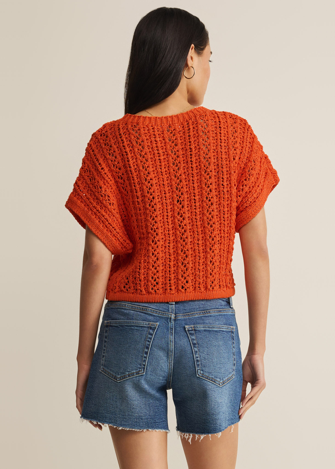 Woman turned around wearing an orange crochet top with denim shorts