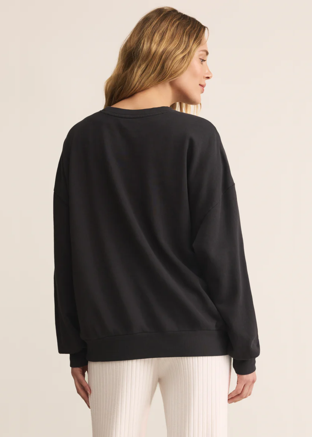 Woman turned around wearing a grey sweatshirt with white pants