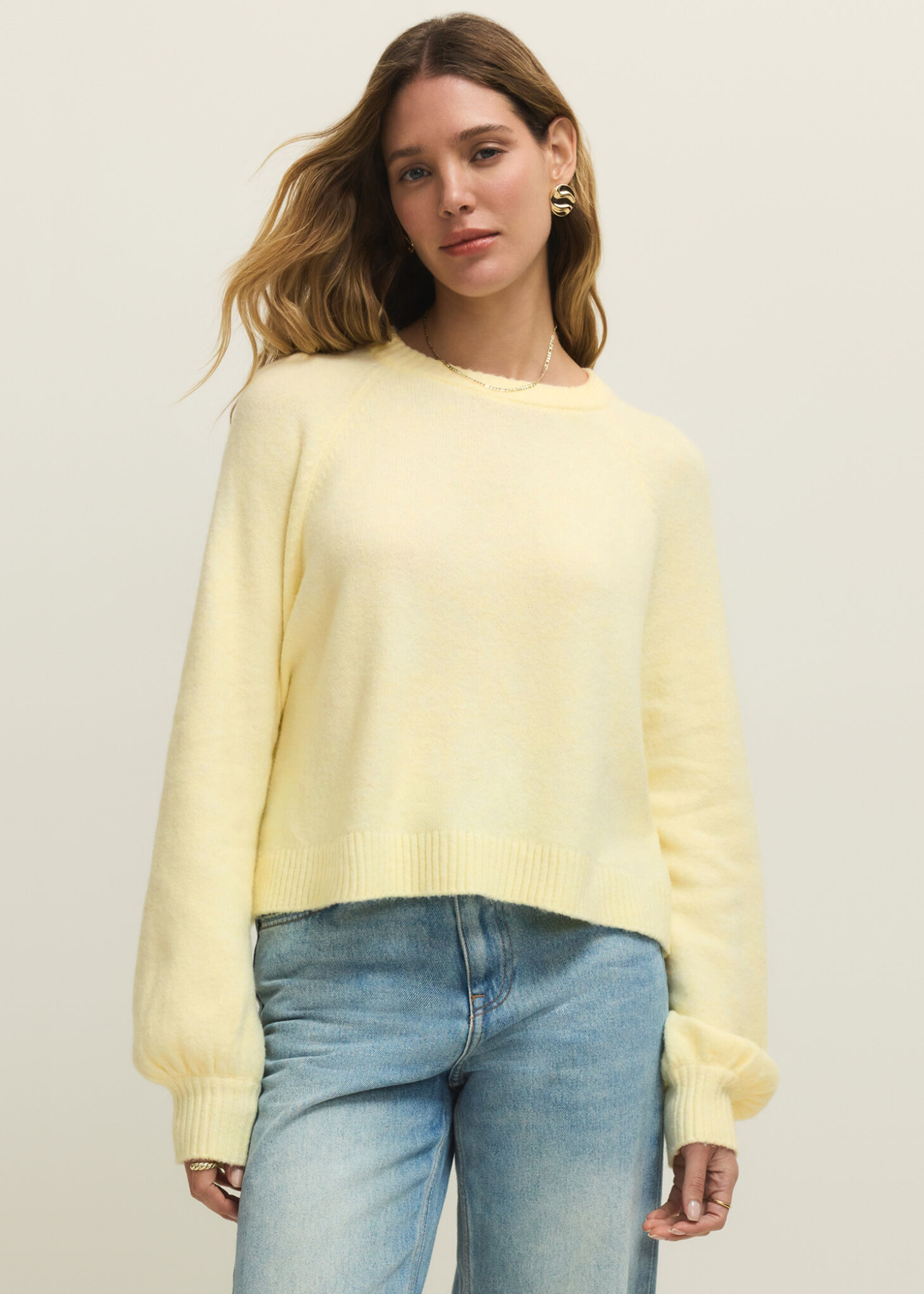 Woman wearing a light yellow sweater with jeans against a white background